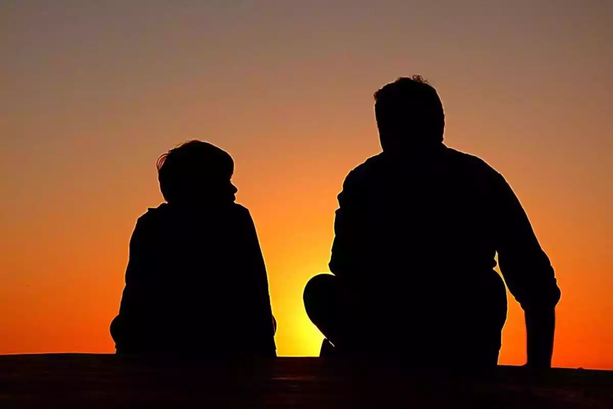 Las siluetas de un padre e un hijo viendo la puesta del sol