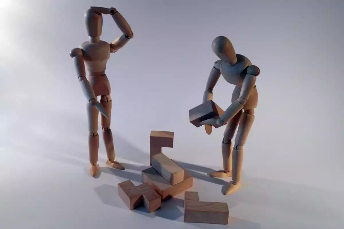 Dos figuras de madera con forma humana resolviendo un problema con varias piezas en el suelo