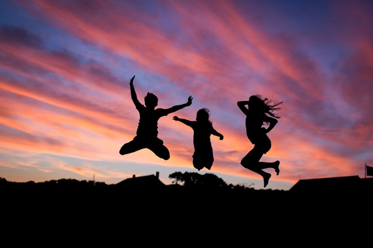 Tres amigos saltando ante un cielo rojizo durante una puesta de sol